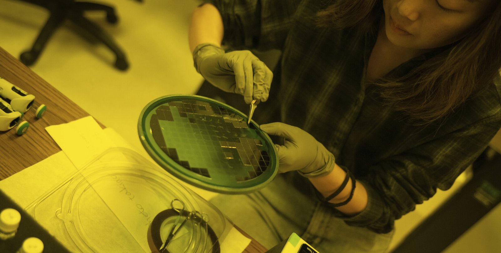 A photo of Wenxin Zhang working with nanoscale materials that appear as pieces of a shiny flat sheet.